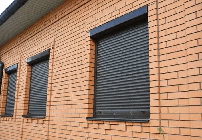 3 dark brown roller shutters on brick wall